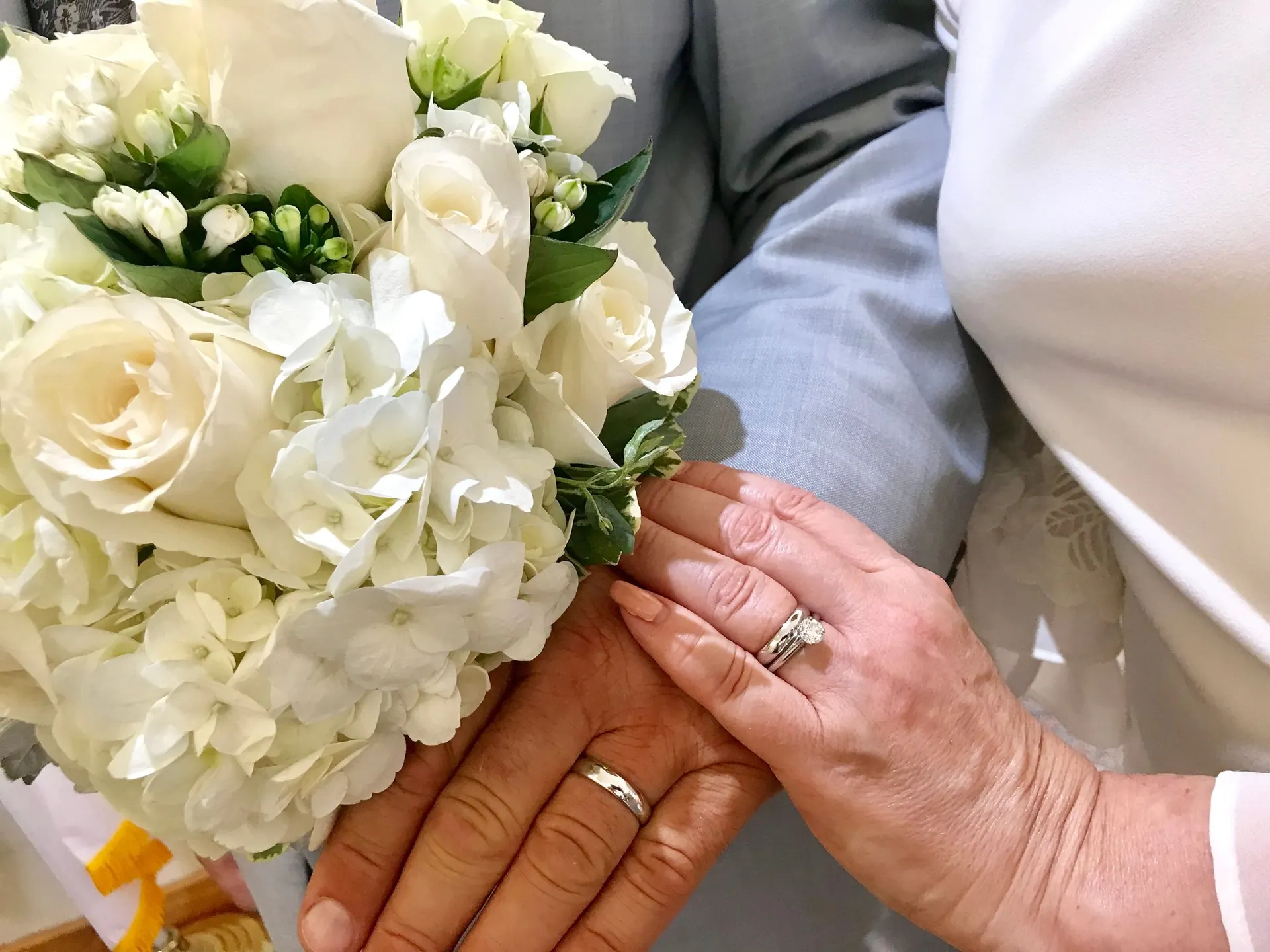 Hände mit Eheringen und weißem Blumenstrauß